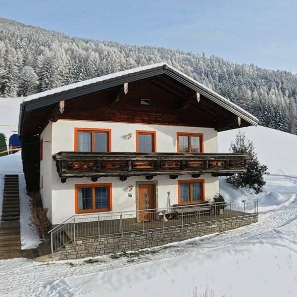 Der Hof von außen im Winter, mit traditioneller Architektur, Balkon und Blick auf die verschneite Berglandschaft.