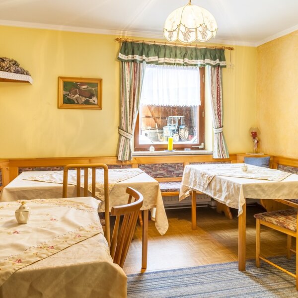 Der Aufenthaltsraum des Bauernhofs mit Holztischen, Sitzbänken und einem Fenster mit Blick auf den Hof.