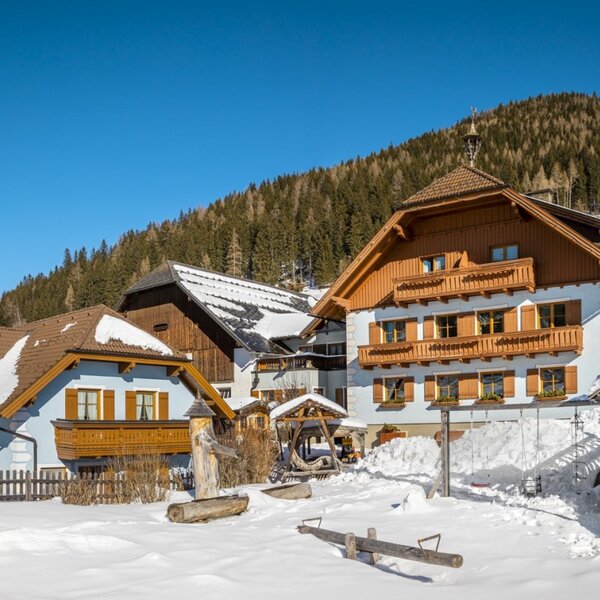 The Farm House buildings and its snow-covered children's play area, set against a winter mountain landscape.