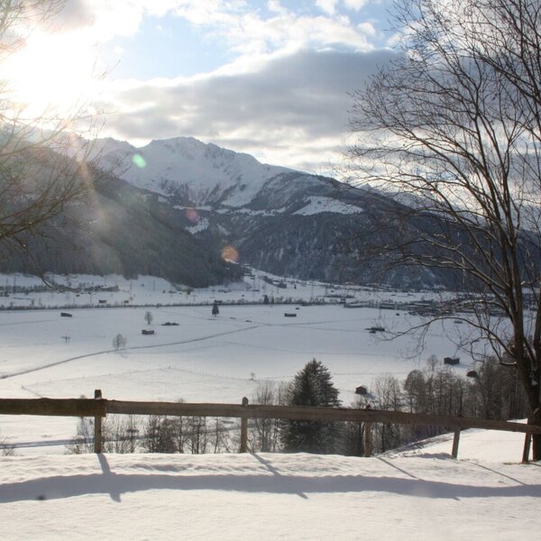 Winterliche Aussicht vom Bauernhof auf das schneebedeckte Tal und die umliegende Bergwelt.