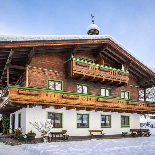Außenansicht des Bauernhofs mit traditioneller Holzfassade und Balkonen, umgeben von winterlicher Schneelandschaft.