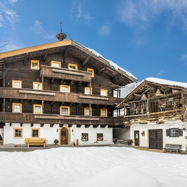 Außenansicht des Bauernhofs mit traditioneller Holzfassade, Balkonen und schneebedecktem Vorplatz.