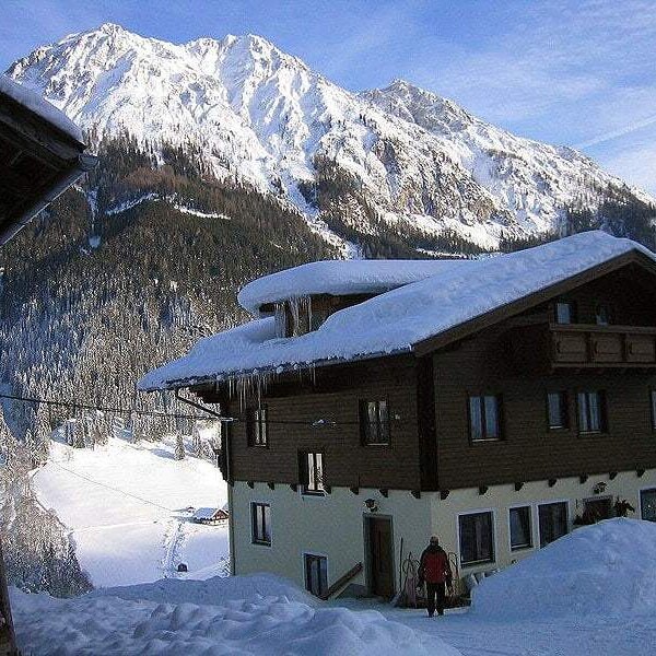 Der Bauernhof im Winter, mit einem Balkon und einer Kulisse aus schneebedeckten Bergen.
