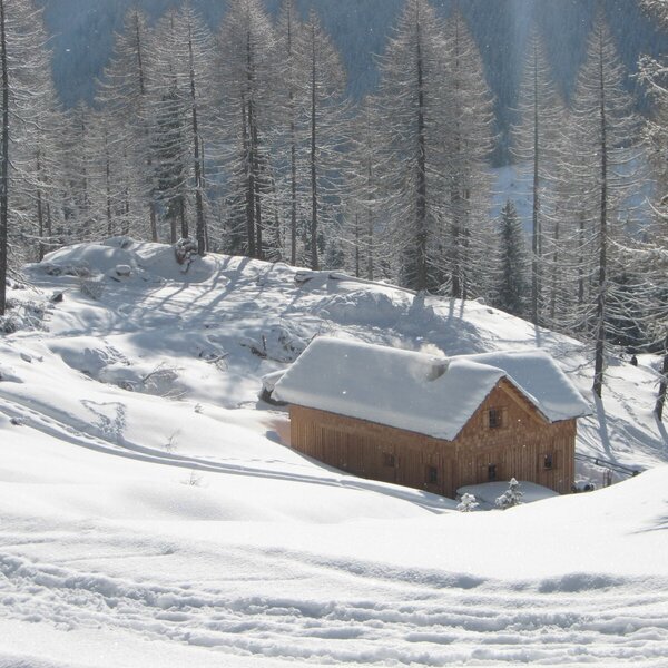 Die verschneite Holzhütte des Hofs in einer Winterlandschaft, mit Rauch aus dem Kamin.