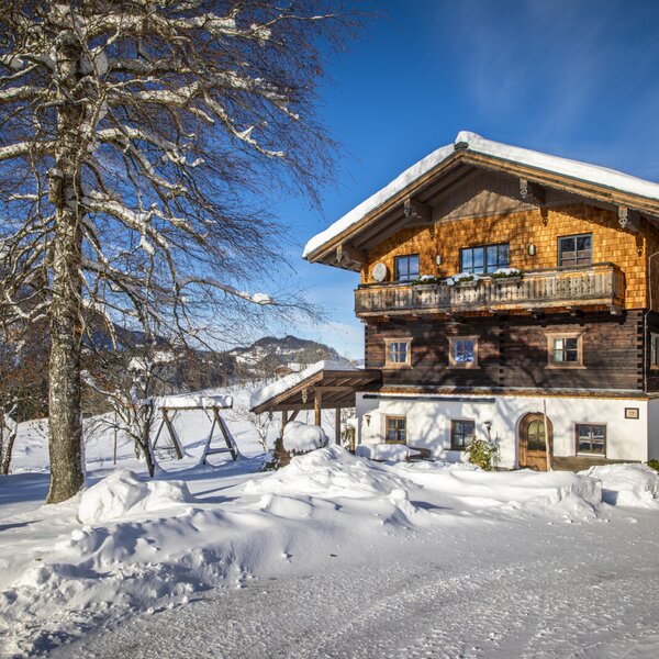 Der schneebedeckte Bauernhof mit traditioneller Holzfassade, Balkonen und Blick auf die umliegenden Berge.