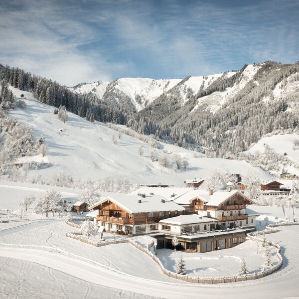 Der Bauernhof in einer schneebedeckten Winterlandschaft, umgeben von Bergen.