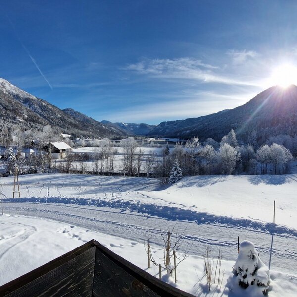 Panoramic winter view from the Farm House, featuring snow-covered fields, mountains, and distant buildings under a bright sky.