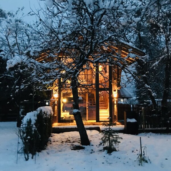The snow-covered farmhouse exterior illuminated by warm indoor lights at dusk.