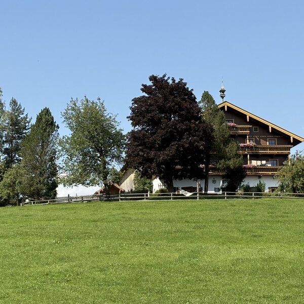 Außenansicht des Bauernhofs mit traditionellem Gebäude, blumengeschmückten Balkonen und grüner Umgebung.