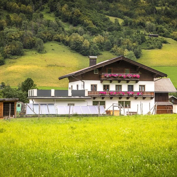 Die einladende Ferienwohnung in traditioneller Holzbauweise, umgeben von einer weitläufigen grünen Wiese vor einer bewaldeten Bergkulisse.