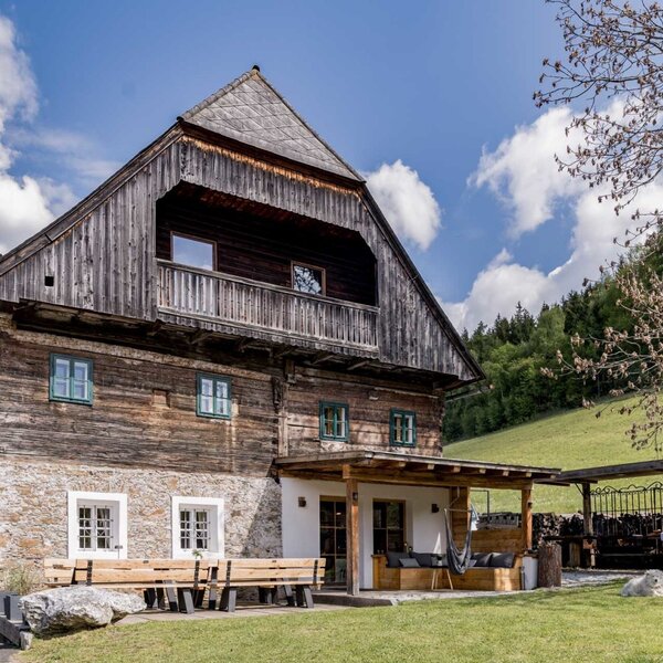Die Außenseite des Bauernhofs mit traditioneller Holz- und Steinfassade, einem Balkon und einer überdachten Terrasse mit Sitzgelegenheiten im Garten.