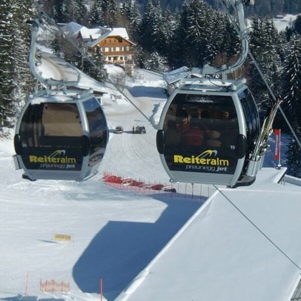 Gondeln der Reiteralm Preunegg Jet Seilbahn über einer schneebedeckten Skipiste mit verschneiten Bäumen.