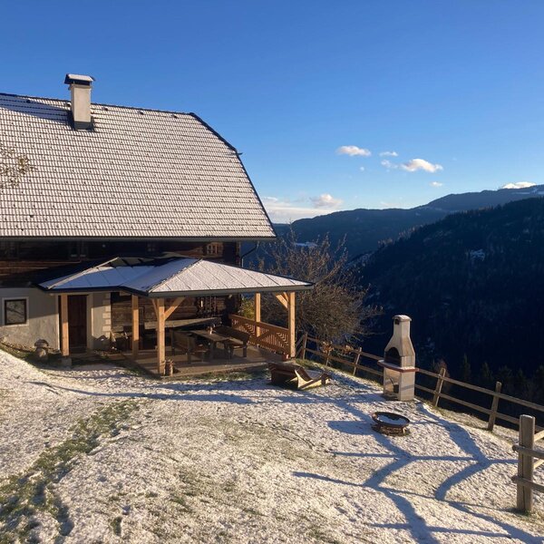 The farmhouse offers a covered outdoor seating area with an adjacent grill and fire pit, set against mountain views and a light dusting of snow.
