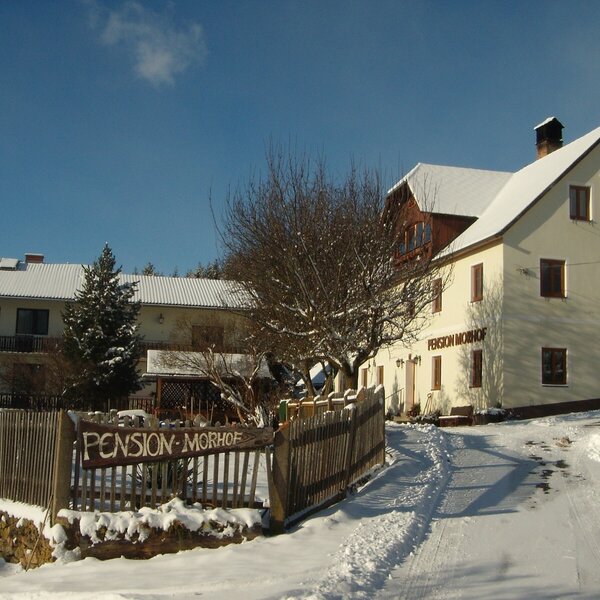 Außenansicht des Bauernhofs 'Pension Morhof' im Winter mit verschneiten Gebäuden und Zufahrtsweg.