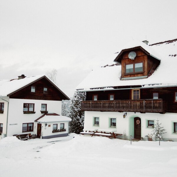 Außenansicht des Bauernhofs im Winter mit schneebedeckten Dächern und Balkonen.