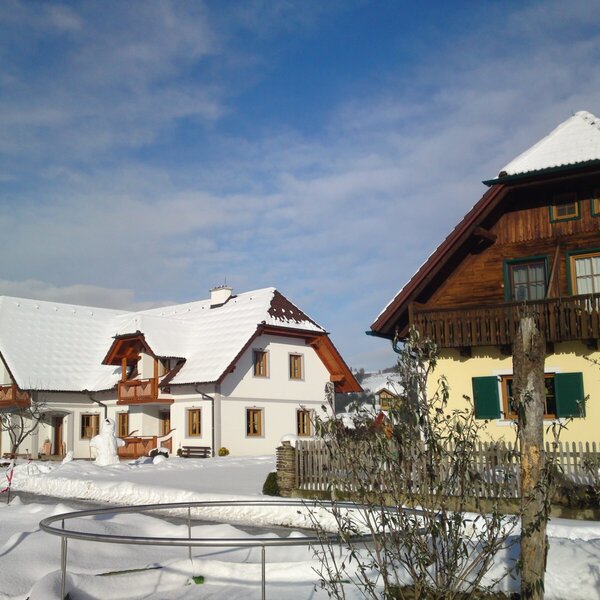 Die Außenansicht des Bauernhofs im Winter, mit schneebedeckten Gebäuden und Dächern.