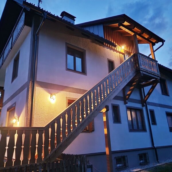 The illuminated exterior of the Farm House, featuring a prominent wooden staircase leading to an upper-level balcony.
