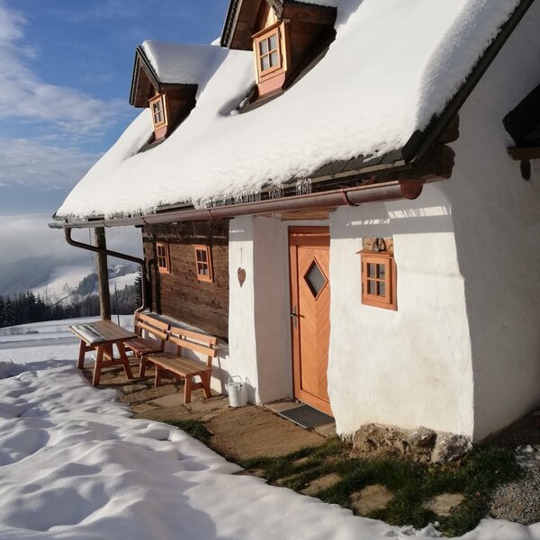 Der schneebedeckte Außenbereich der Ferienhütte mit einer Holzbank und einem Tisch am Eingang.