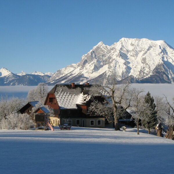 The Farm House surrounded by snow, with a children's playground, and snowy mountains towering above a cloud-filled valley.