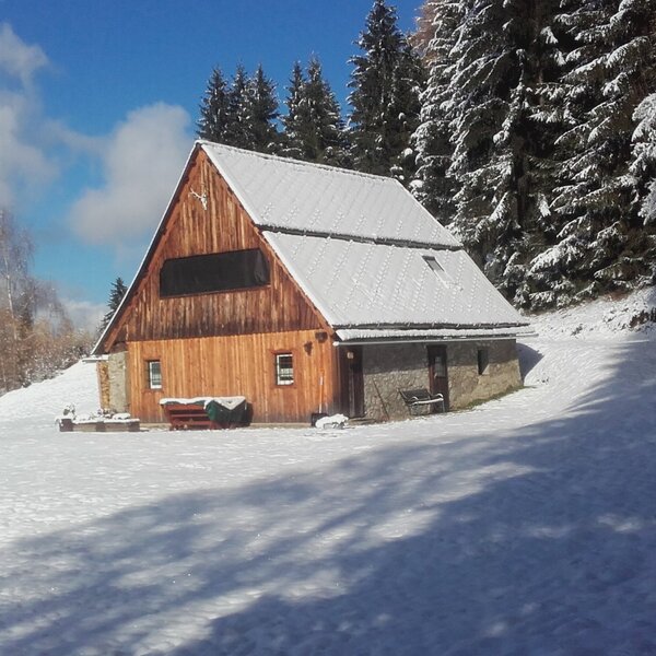 Der Hof mit Holzfassade und Steinsockel in einer verschneiten Winterlandschaft, umgeben von einem Nadelwald.