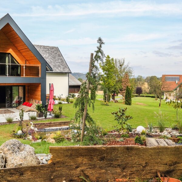 The Farm House features a contemporary exterior with a ground-floor patio and an upper-level balcony, set within a spacious garden that includes a small pond.
