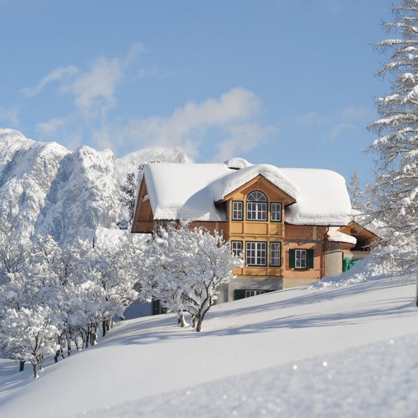 Der schneebedeckte Bauernhof liegt eingebettet in eine Winterlandschaft mit verschneiten Bergen im Hintergrund.