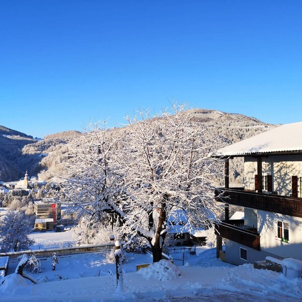 Der schneebedeckte Bauernhof mit Balkonen und Blick auf das Dorf und die verschneiten Berge.