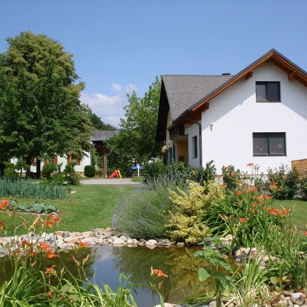 Der Bauernhof mit Zierteich, Gemüsegarten und Spielplatz im Hintergrund.