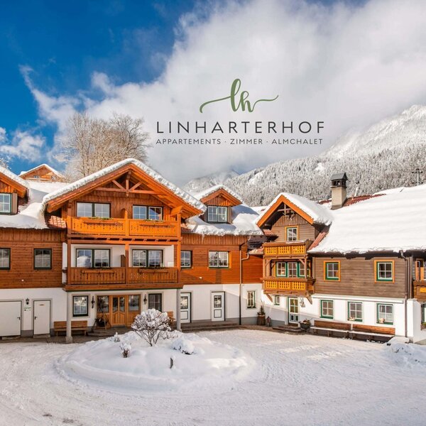 Die schneebedeckte Außenansicht des Bauernhofs Linharterhof vor einer winterlichen Bergkulisse.