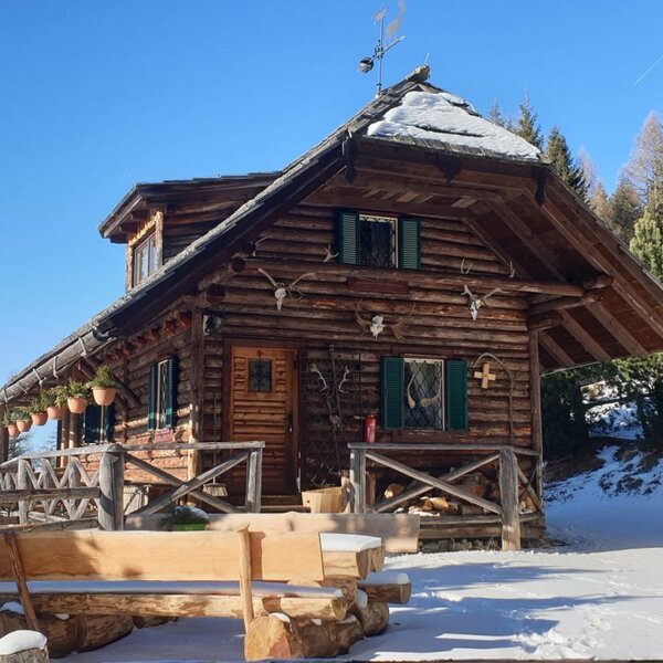 Der Hof als traditionelles Holzhaus, umgeben von Schnee, mit einer Holzbank vor dem Eingang.