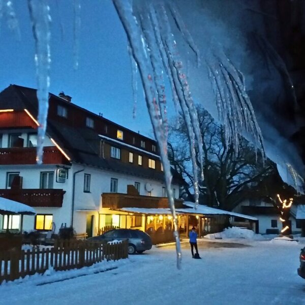 Außenansicht des Bauernhofs im Winter bei Dunkelheit, mit beleuchteter Fassade, Schnee und Eiszapfen.