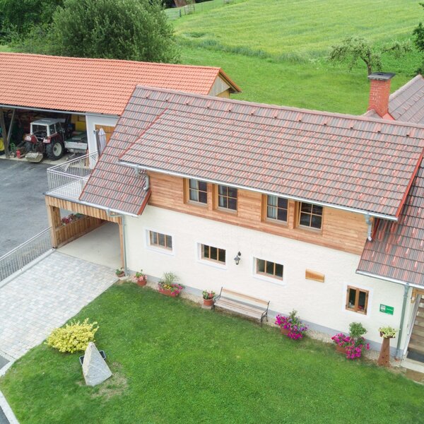 Außenansicht des Bauernhofs mit rotem Ziegeldach, weißer Fassade, grünem Rasen und Carport.