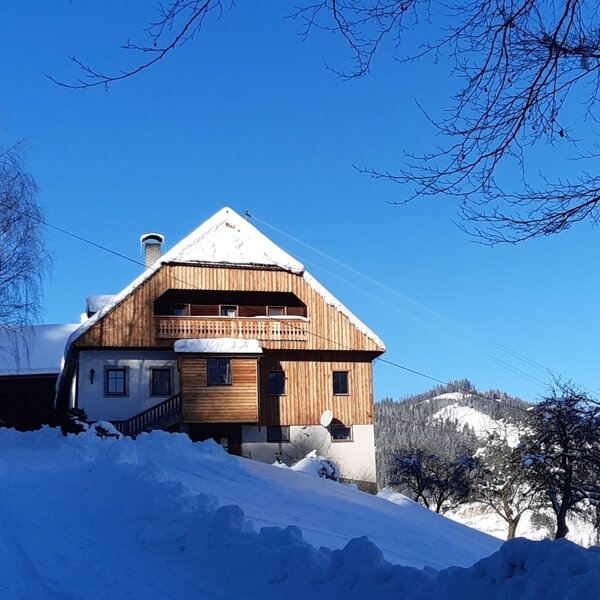 The farmhouse exterior with its wooden facade and balcony, set in a snowy landscape with distant mountains.