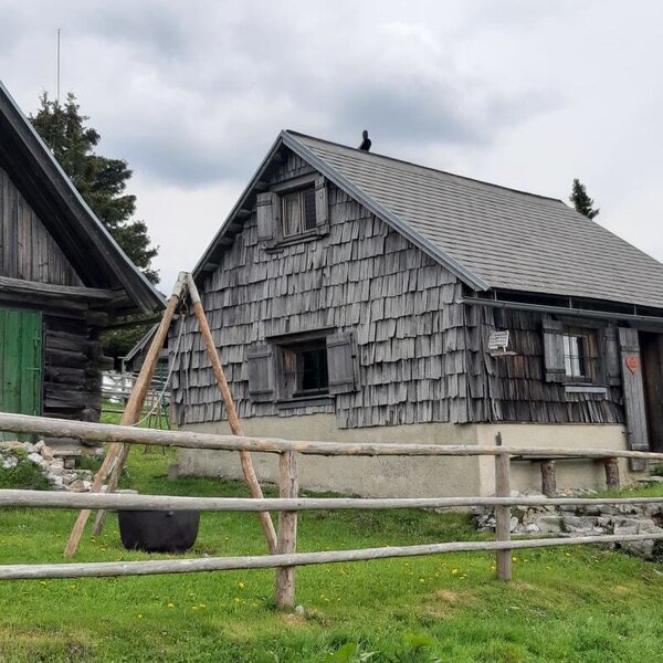 The farmhouse exterior displays two traditional wooden buildings, one with green shutters and another with shingled walls, enclosed by a wooden fence.