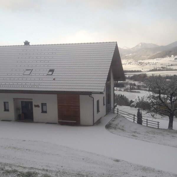 Der Bauernhof im Winter, umgeben von Schnee, mit Blick auf das Tal und die Berge.