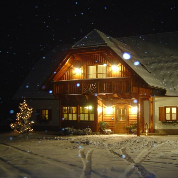 The farmhouse exterior illuminated at night, featuring snow-covered grounds and a decorated Christmas tree.