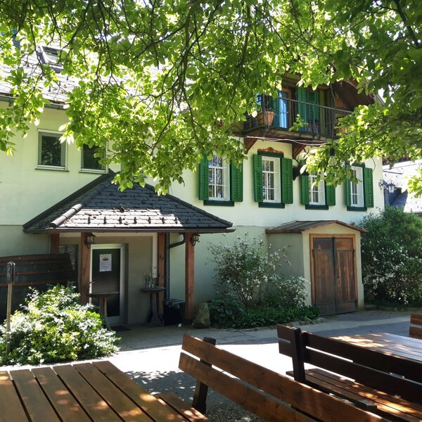 Die Außenansicht des Hofes mit grünen Fensterläden, einem Balkon und einem Sitzbereich im Freien mit Holzbänken und Tischen.