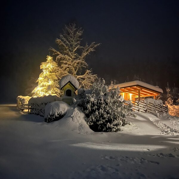 Das Ferienhaus im Winter bei Nacht, mit verschneiter Landschaft und beleuchteten Bäumen.