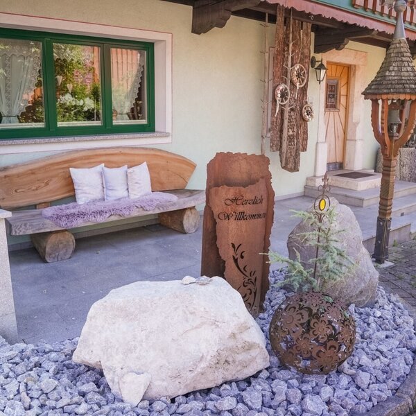 Der Eingangsbereich des Bauernhofs mit einer Holzbank, einem Willkommensschild und traditionellen Dekorationen.