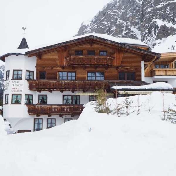 Außenansicht des Bauernhofs im Winter, umgeben von Schnee und Bergen, mit traditioneller Holzfassade und Balkonen.