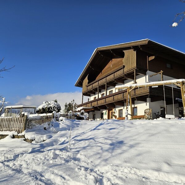 Der Bauernhof im Winter, mit einer schneebedeckten Fassade, Holzbalkonen und einem Spielgerüst.