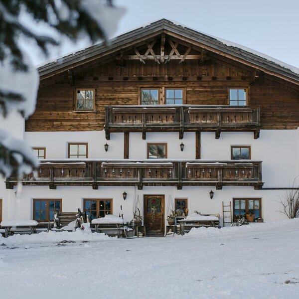 The Farm House exterior in winter, featuring traditional wooden balconies and snow-covered ground.