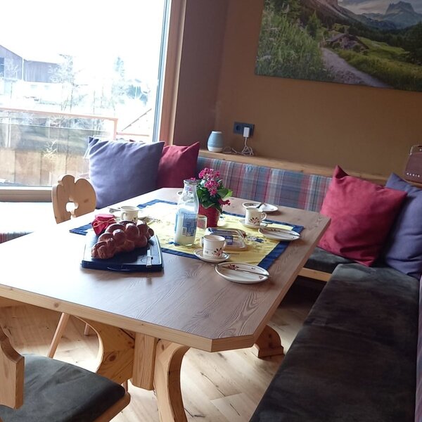 Frühstücksbereich auf dem Bauernhof mit Holztisch, Sitzbänken und Frühstücksgedeck am Fenster.