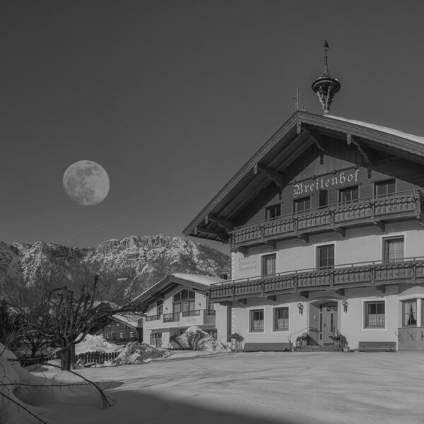 Der Bauernhof "Breitenhof" im Winter mit verschneiten Bergen und Vollmond.
