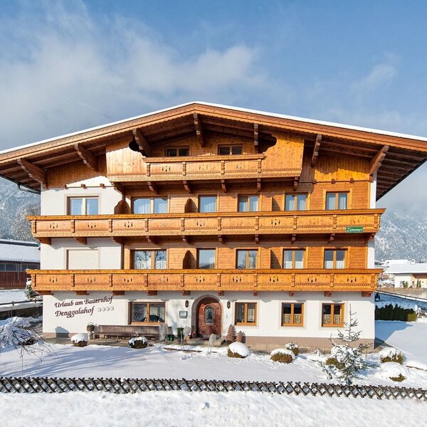 The exterior of the farm house, featuring multiple wooden balconies and surrounded by a snow-covered landscape.