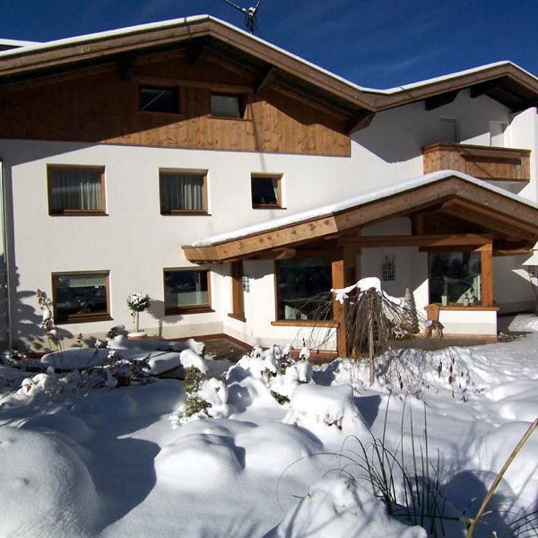 The Farm House exterior, featuring white walls, wooden accents, and a covered entrance, surrounded by snow.