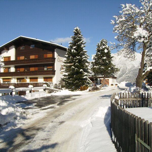 Der Bauernhof in verschneiter Winterlandschaft mit Zugangsweg und Blick auf die Berge.