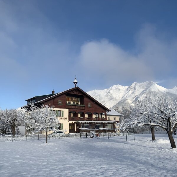 Der Bauernhof im Winter, umgeben von schneebedeckten Obstbäumen des Anwesens und mit Blick auf die umliegenden Berge.