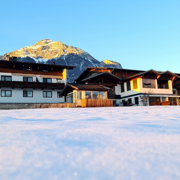 Außenansicht des Bauernhofs im Winter, mit verschneiter Landschaft und einem Berg im Hintergrund.