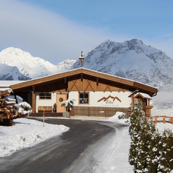 Esterno degli Ap­par­te­ments con facciata in legno, montagne innevate sullo sfondo e un vialetto.